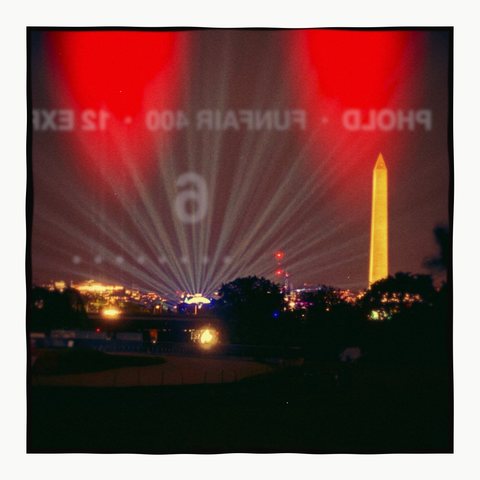 Searchlights around a monument at night, with red light leaks and the backing paper's numbers showing through